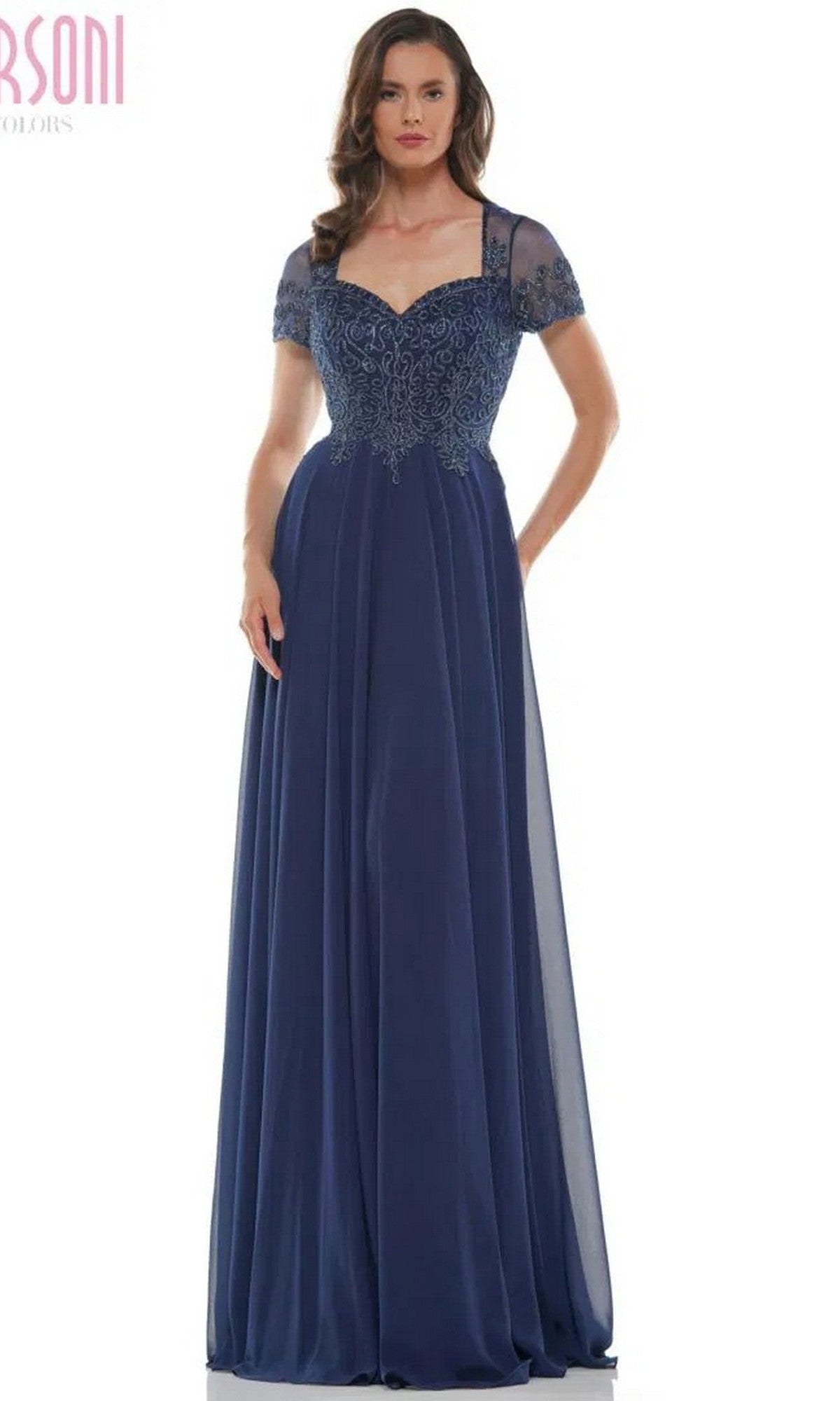 A woman wearing the Marsoni M271 long formal dress in navy, featuring a sweetheart neckline, short sheer sleeves, lace-embroidered bodice, and a flowing pleated chiffon skirt.